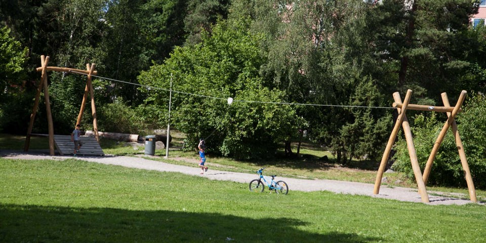 Barn leker med en linbana i en park omgivna av grönt gräs och grönskande träd.